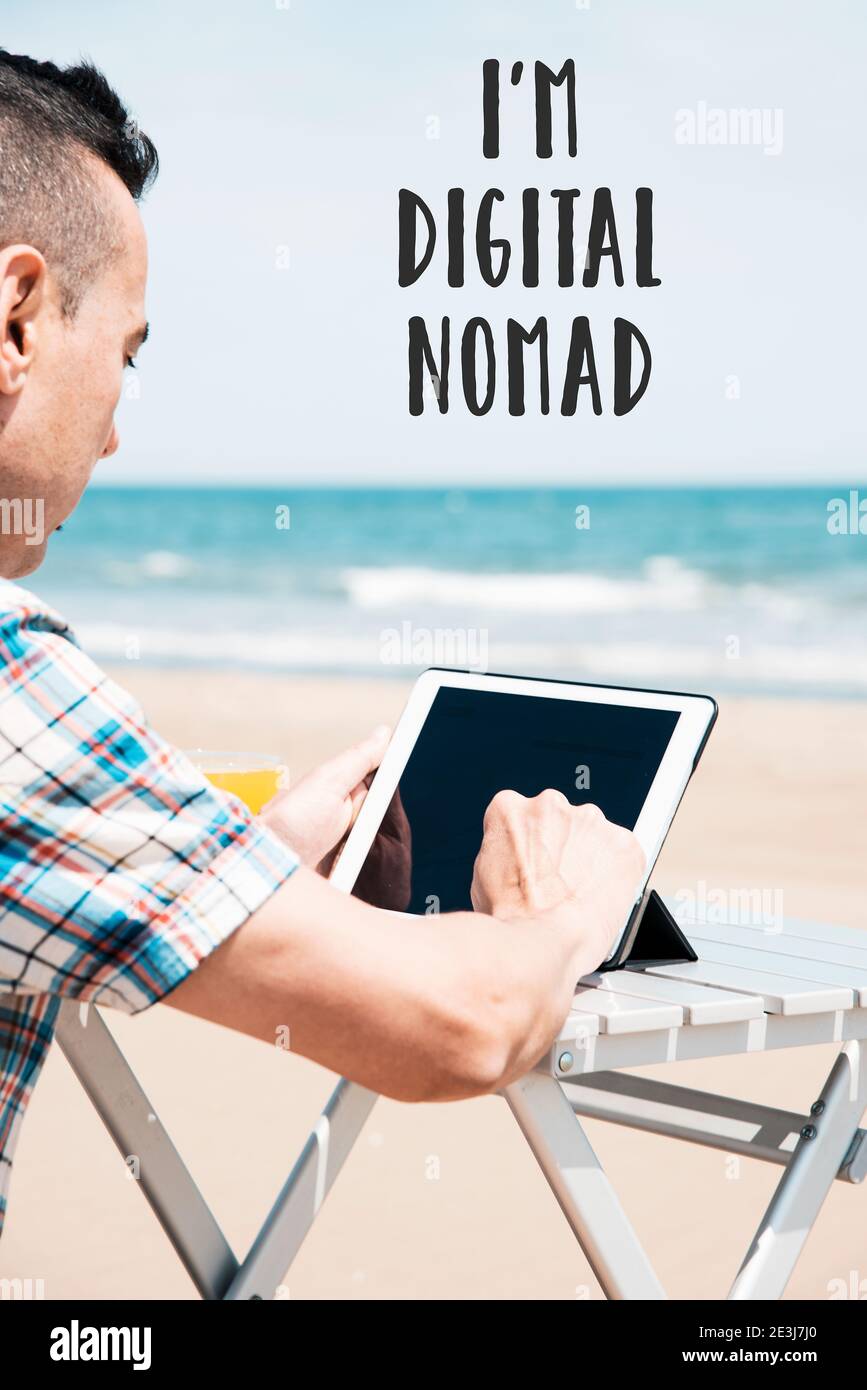 Il testo sono un nomade digitale e un giovane caucasico sulla spiaggia, utilizzando un tablet digitale, seduto ad un tavolo all'aperto, con l'oceano sul retro Foto Stock