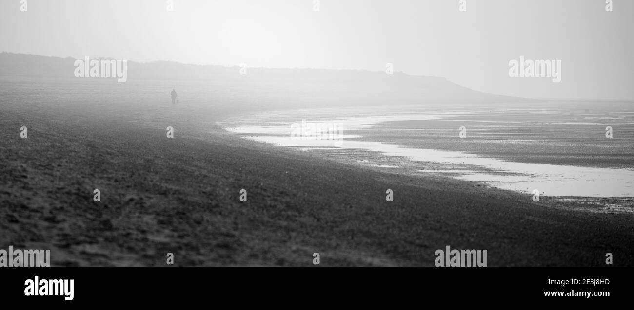 Una figura sola su una spiaggia nebbiosa in inverno. Foto Stock