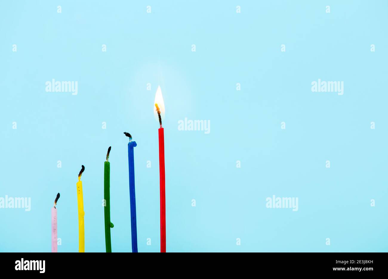 Gruppo di candele bruciate e una rossa alta che brucia su sfondo azzurro. Idea, concetto di successo. Molto spazio per la copia. Foto Stock