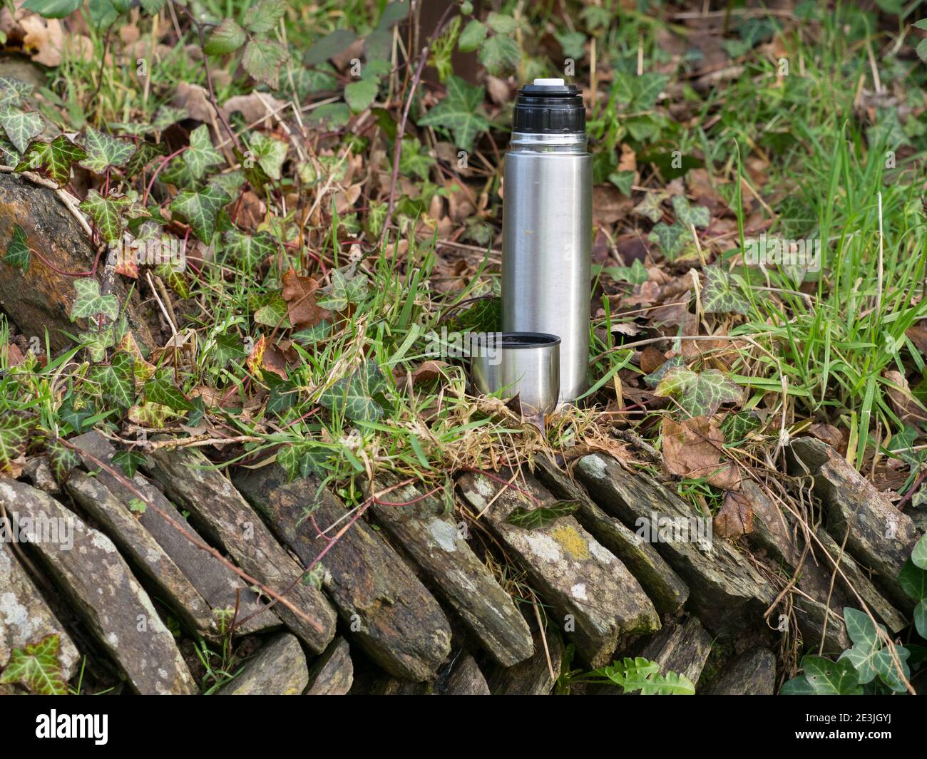 Una matraccio di metallo d'argento e una tazza si trovano su una pietra Muro in un setting.Cornwall.UK rurale Foto Stock