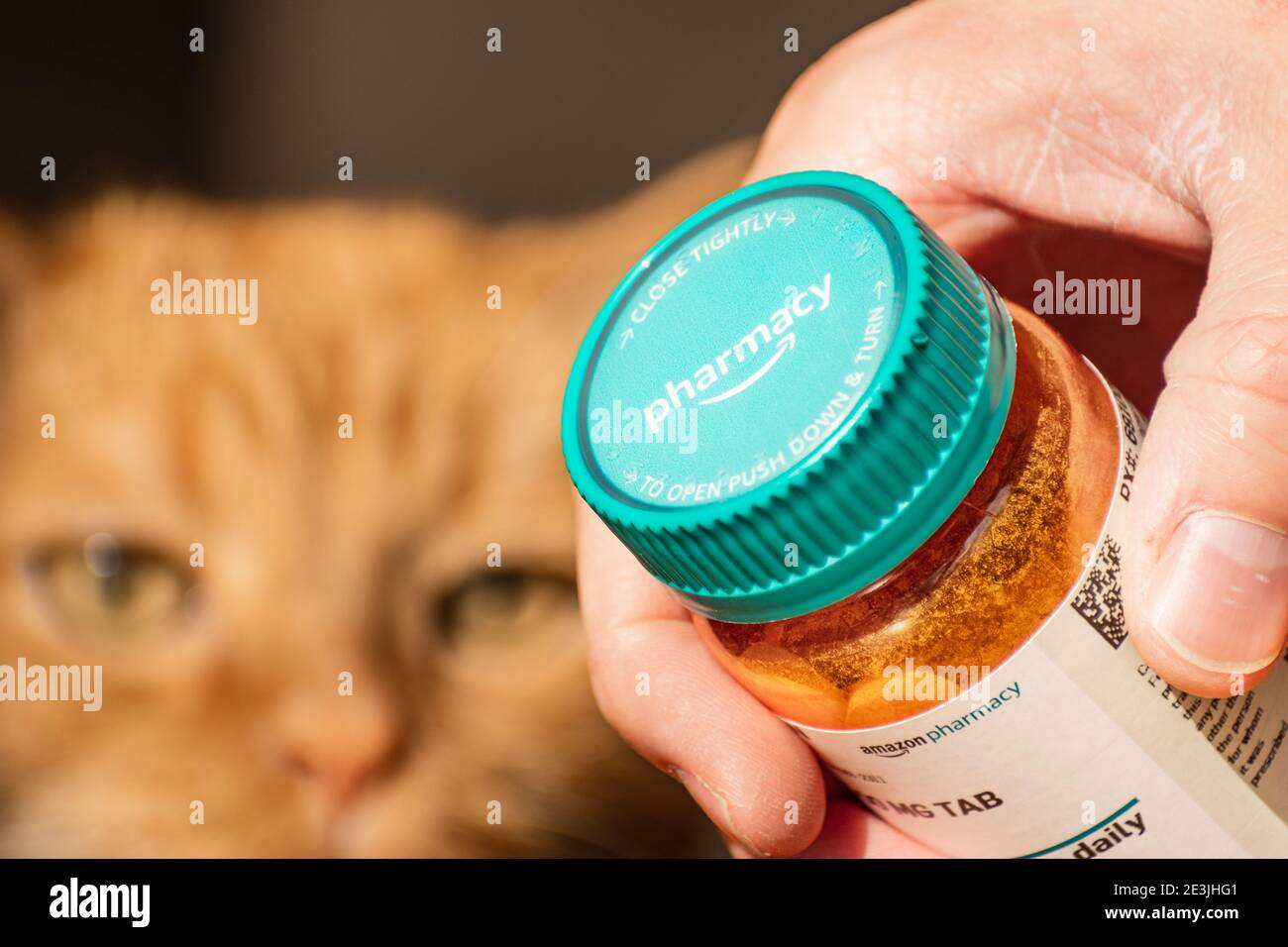 Mano che tiene una bottiglia di Amazon Pharmacy Rx; faccia del gatto sfocata visibile sullo sfondo; Amazon Pharmacy è una farmacia online americana, filiale di A. Foto Stock