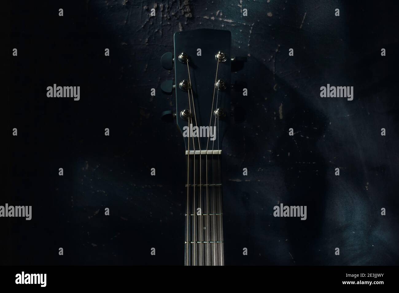 Una chitarra acustica si erge contro il muro contro uno sfondo scuro. Foto Stock