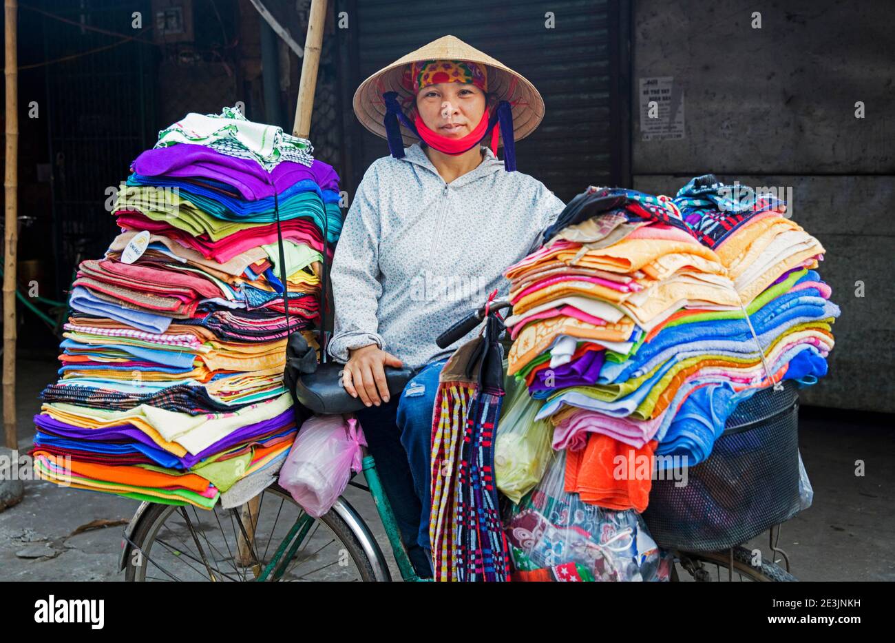 Donna vietnamita con cappello conico nón Lá che vende tessuti e. Vestiti da bicicletta nella città Ninh Binh nel Delta del fiume Rosso del Vietnam settentrionale Foto Stock