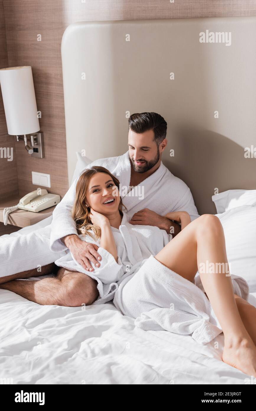 Un uomo sorridente che abbracciava la fidanzata in accappatoio sul letto  dell'hotel camera Foto stock - Alamy
