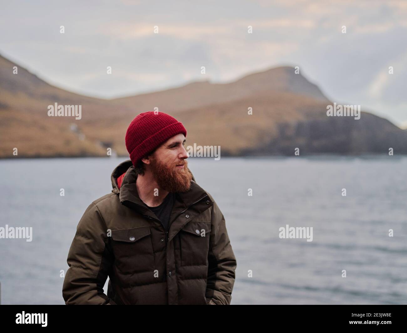 Uomo bearded in bania rossa e giacca in piedi vicino all'oceano Foto Stock