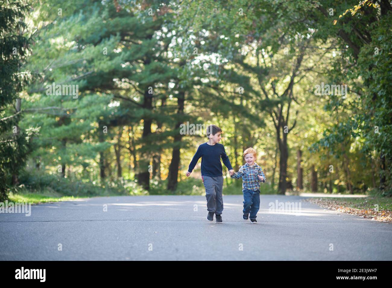 Fratelli che tengono felicemente le mani che corrono lungo una strada alberata Foto Stock