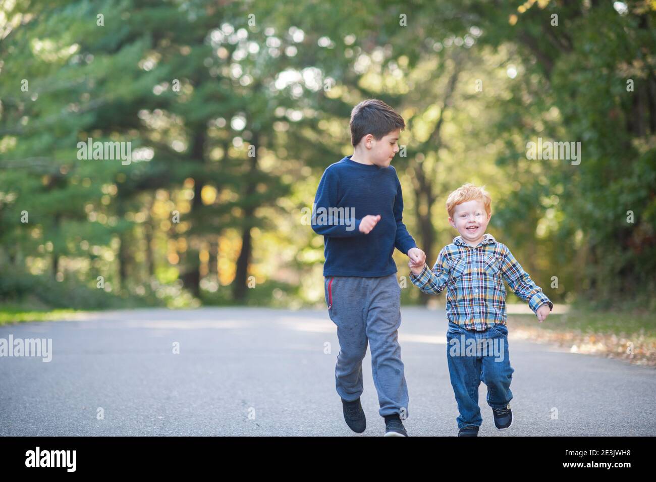 Due fratelli che corrono lungo una strada mentre le mani sorridono Foto Stock