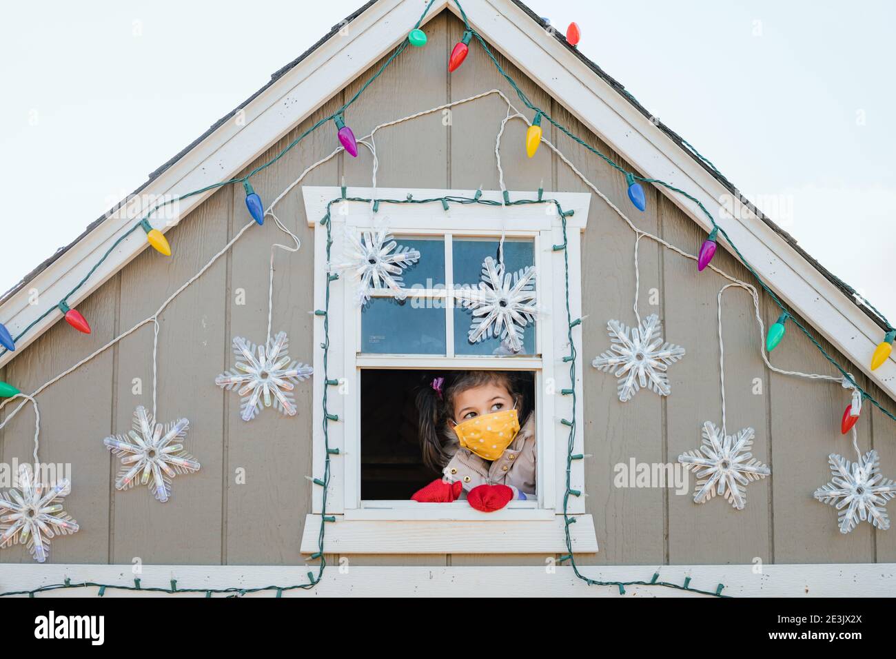 Ragazza giovane in maschera di faccia guardando fuori le decorazioni di natale della finestra Foto Stock