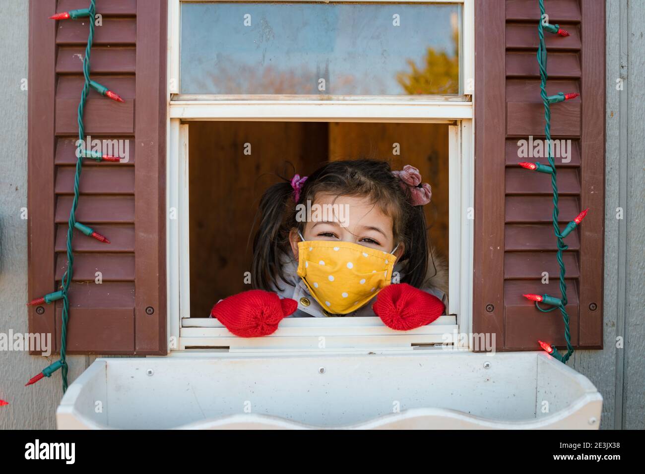 Giovane ragazza guardando attraverso la finestra con maschera viso luci di natale Foto Stock