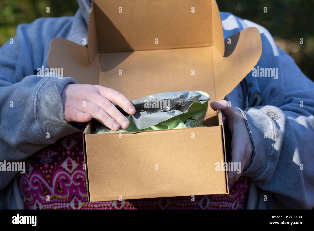 Donna che apre una borsa di plastica verde in una scatola di cartone Foto Stock