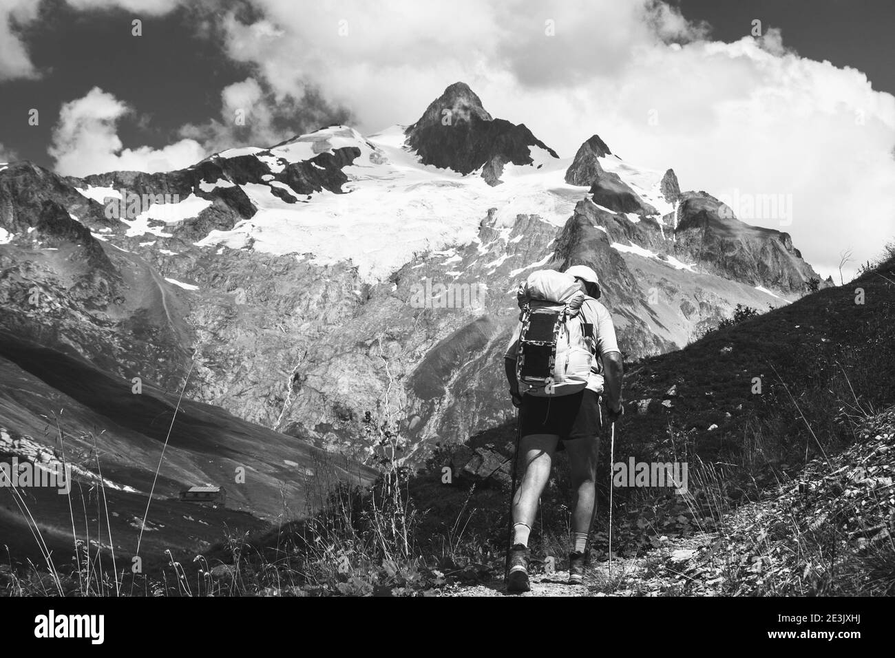 Uomo anziano trekking Alpi francesi in estate con zaino solare. L'Aiguille des Glaciers, montagna nel massiccio del Monte Bianco. Vista dalla valle di Chapieux, Foto Stock