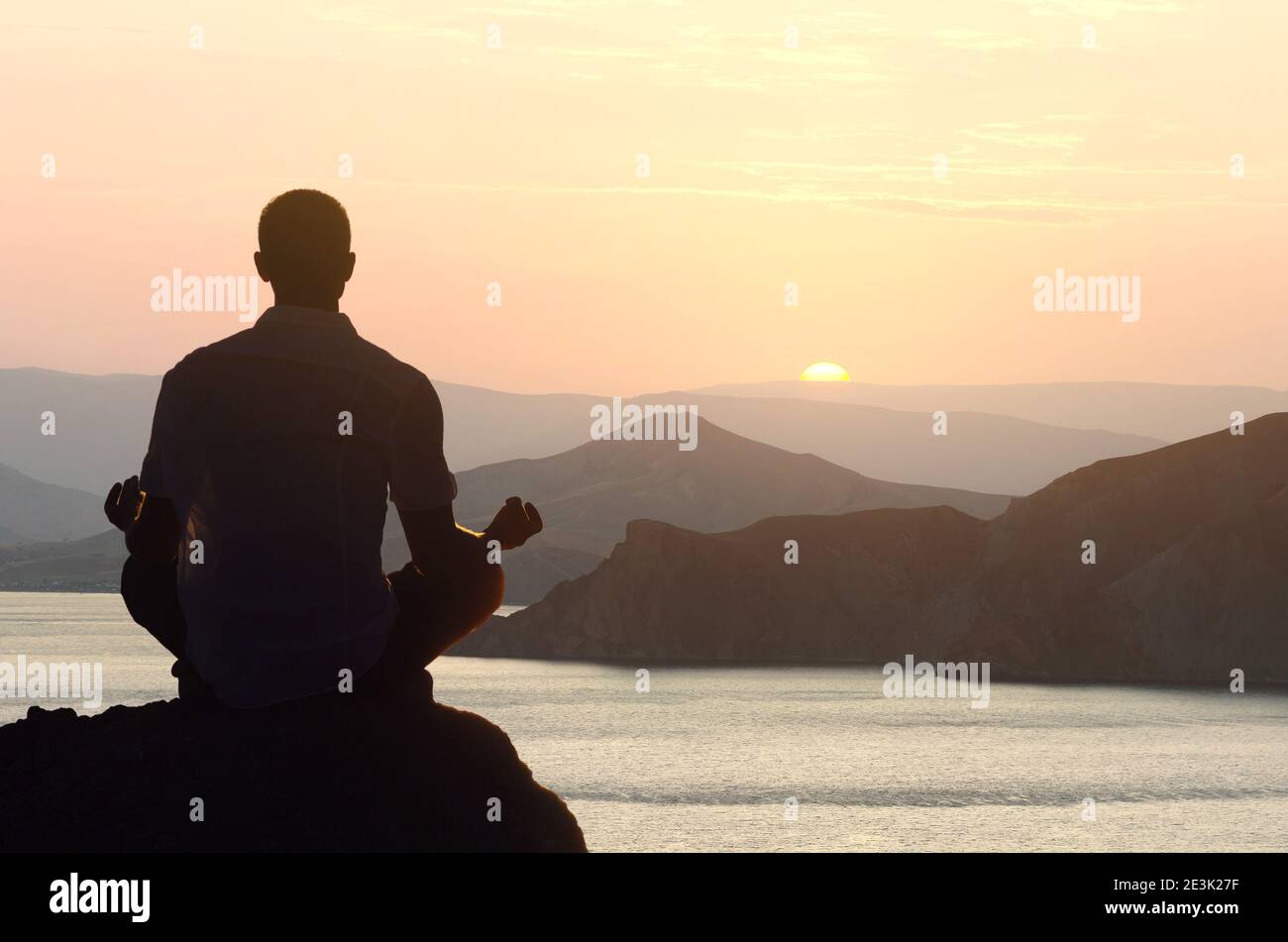 Silhouette di un uomo meditando yoga all'alba in un lotus posizione sul mare Foto Stock