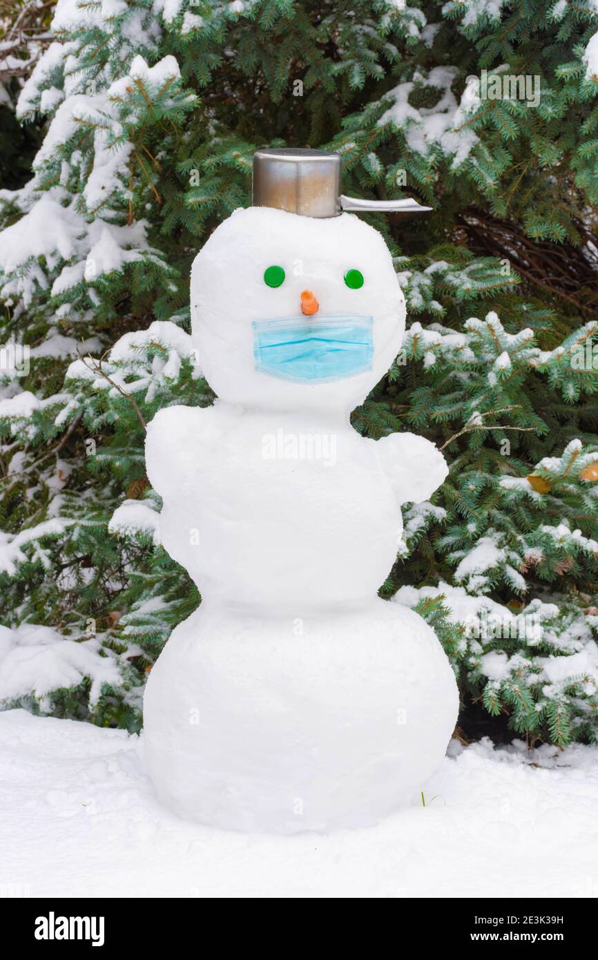 Simpatico snowman all'aperto nel parco in una giornata invernale innevata, indossando una maschera medica a causa di Coronavirus Covid 19 nuova realtà e vita normale Foto Stock