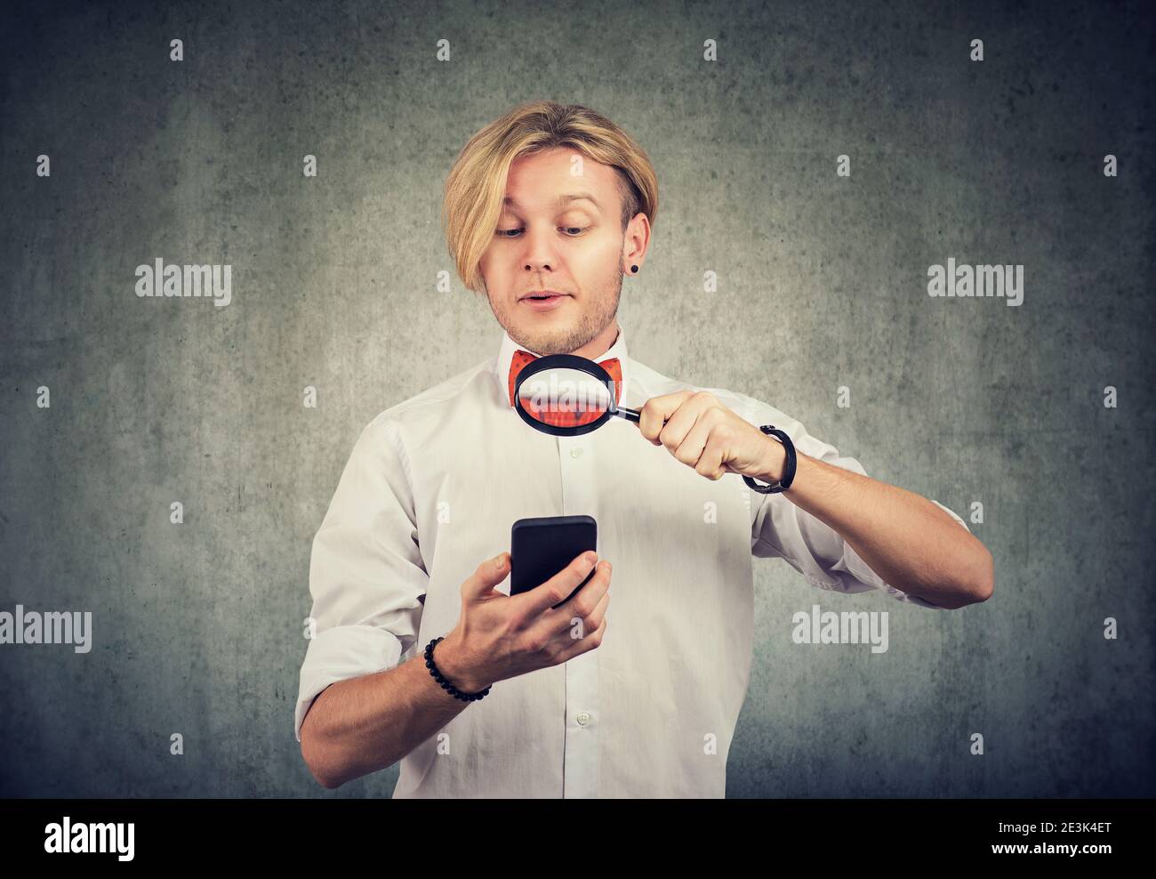 Ritratto di un giovane curioso che usa il cellulare con lente di ingrandimento Foto Stock