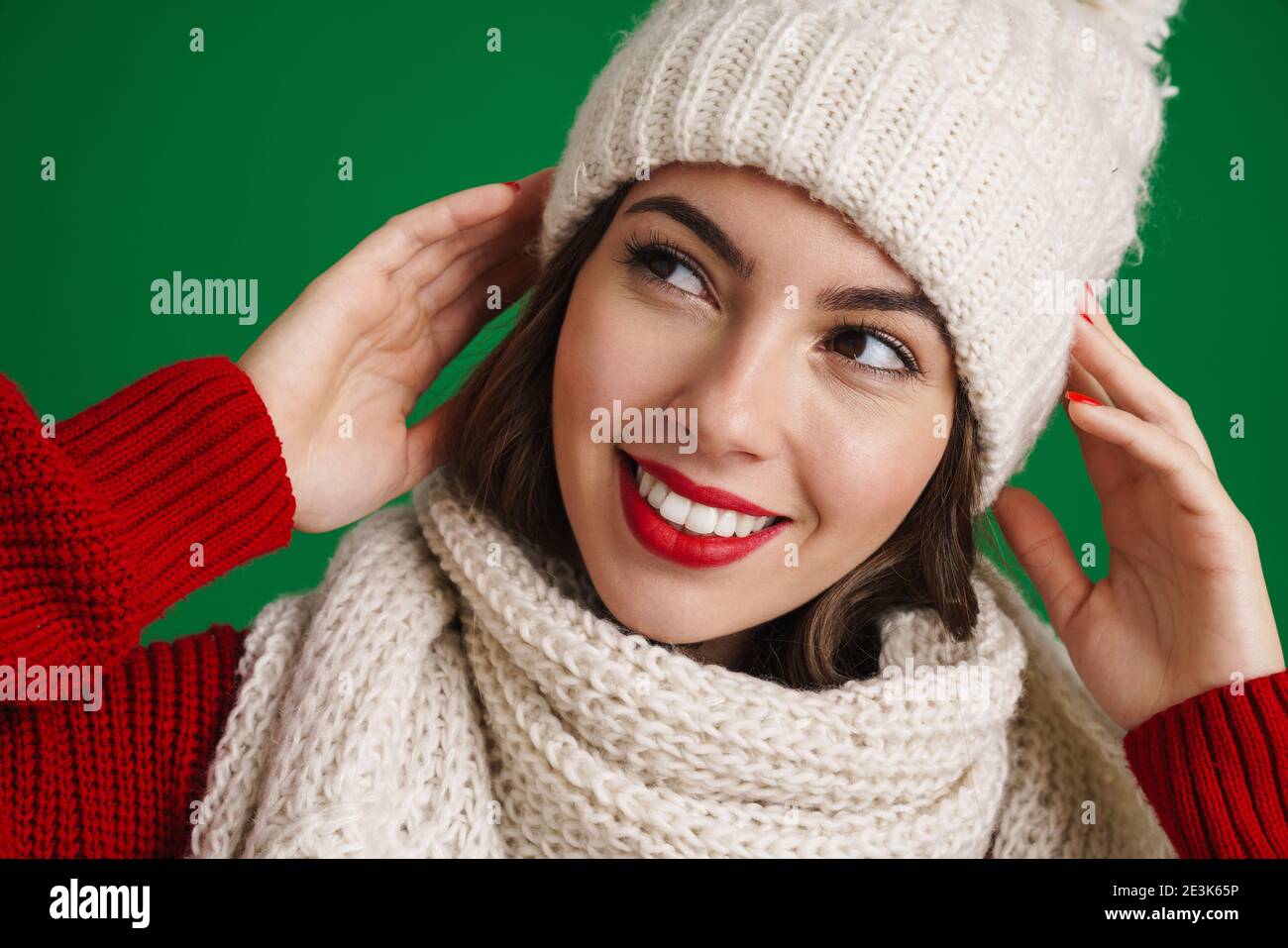 Bella ragazza felice in cappello a maglia e sciarpa sorridente a. telecamera isolata su sfondo verde Foto Stock