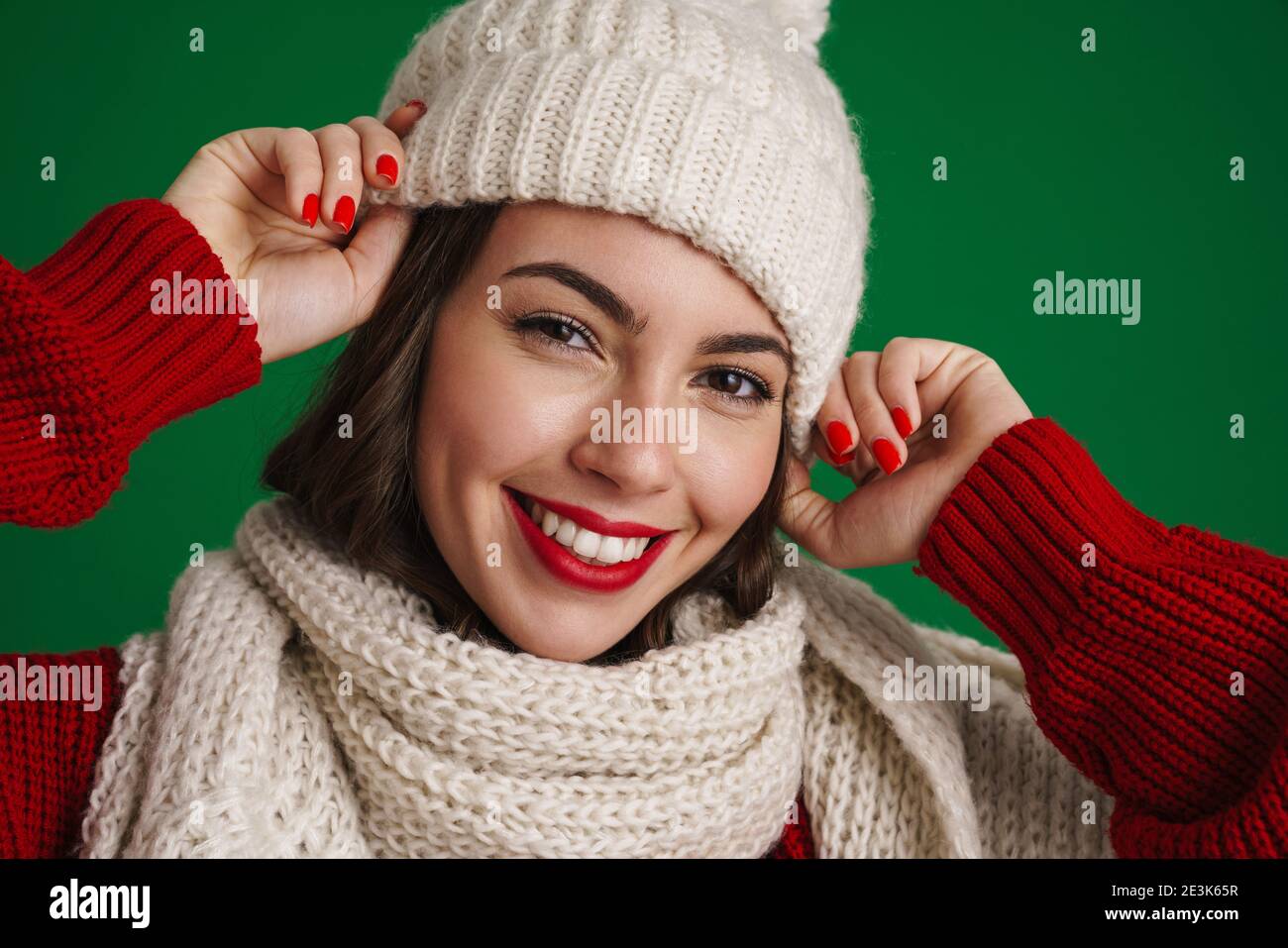 Bella ragazza felice in cappello a maglia e sciarpa sorridente a. telecamera isolata su sfondo verde Foto Stock