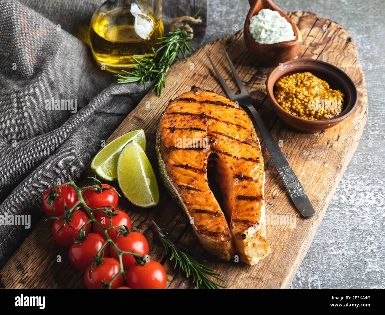 bistecca di salmone di pesce alla griglia, trota in un vecchio bordo di legno, spezie, rosmarino, pomodoro, Foto Stock