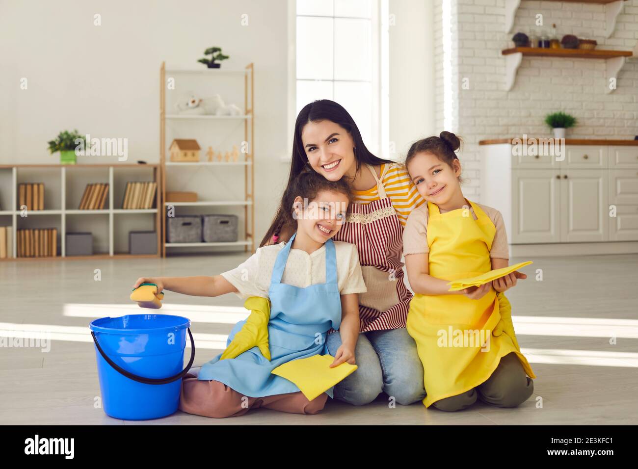 Felice madre e figlie in grembiuli seduti a pavimento con tele da pavimento e sorridendo alla macchina fotografica Foto Stock