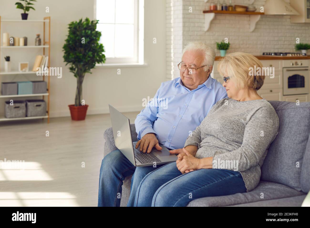 Coppia senior seduta sul divano nel soggiorno e che legge notizie o guarda film sul computer portatile. Foto Stock