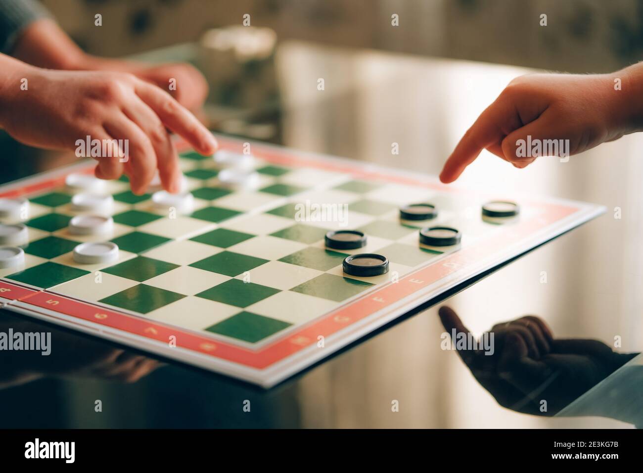 Primo piano di due mani di bambini 'che giocano bozze gioco da tavolo a casa. Foto Stock