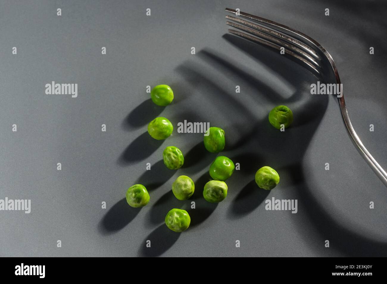 Dieta dura con alcuni piselli verdi e una forchetta con ombre su uno sfondo grigio con spazio di copia, concetto astratto moderno per la risoluzione di mangiare vegetariano Foto Stock