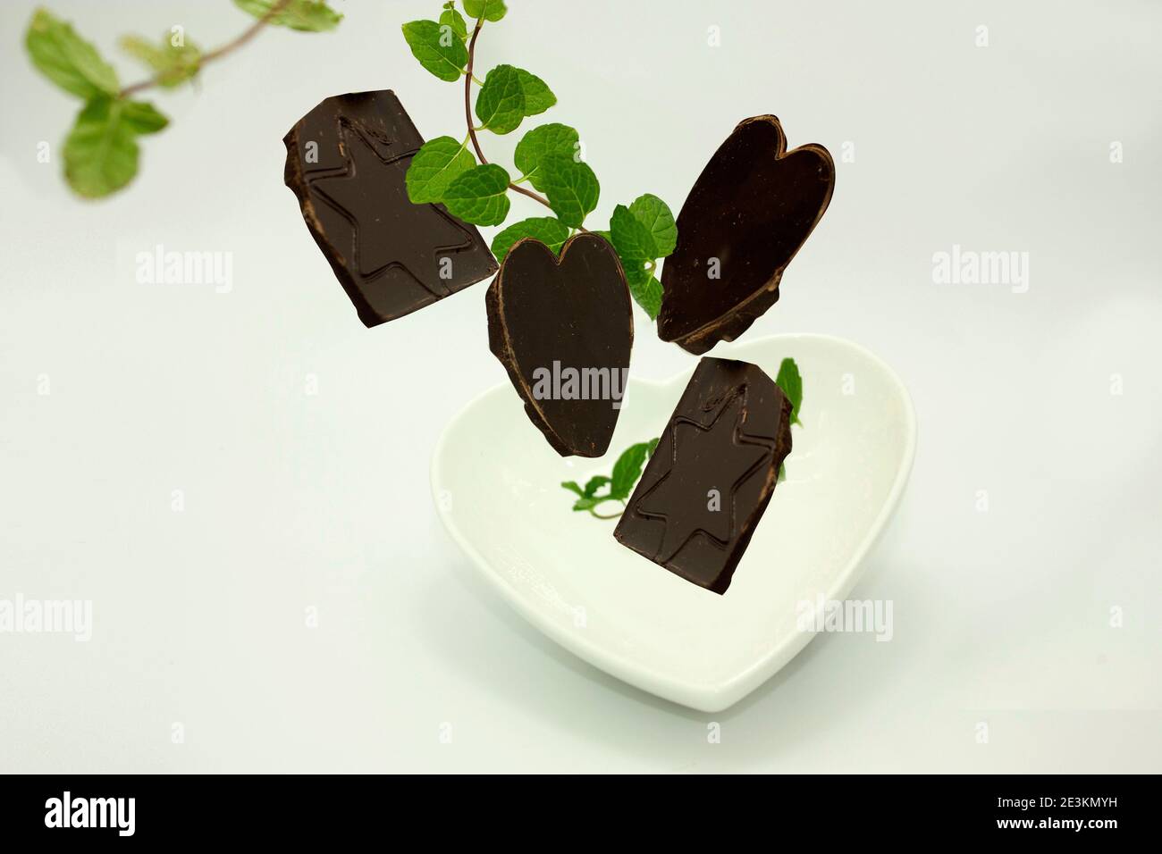 Cioccolato grossolano inciso a forma di cuore e stella, cadente tra foglie di menta fresca in una ciotola bianca in ceramica Foto Stock