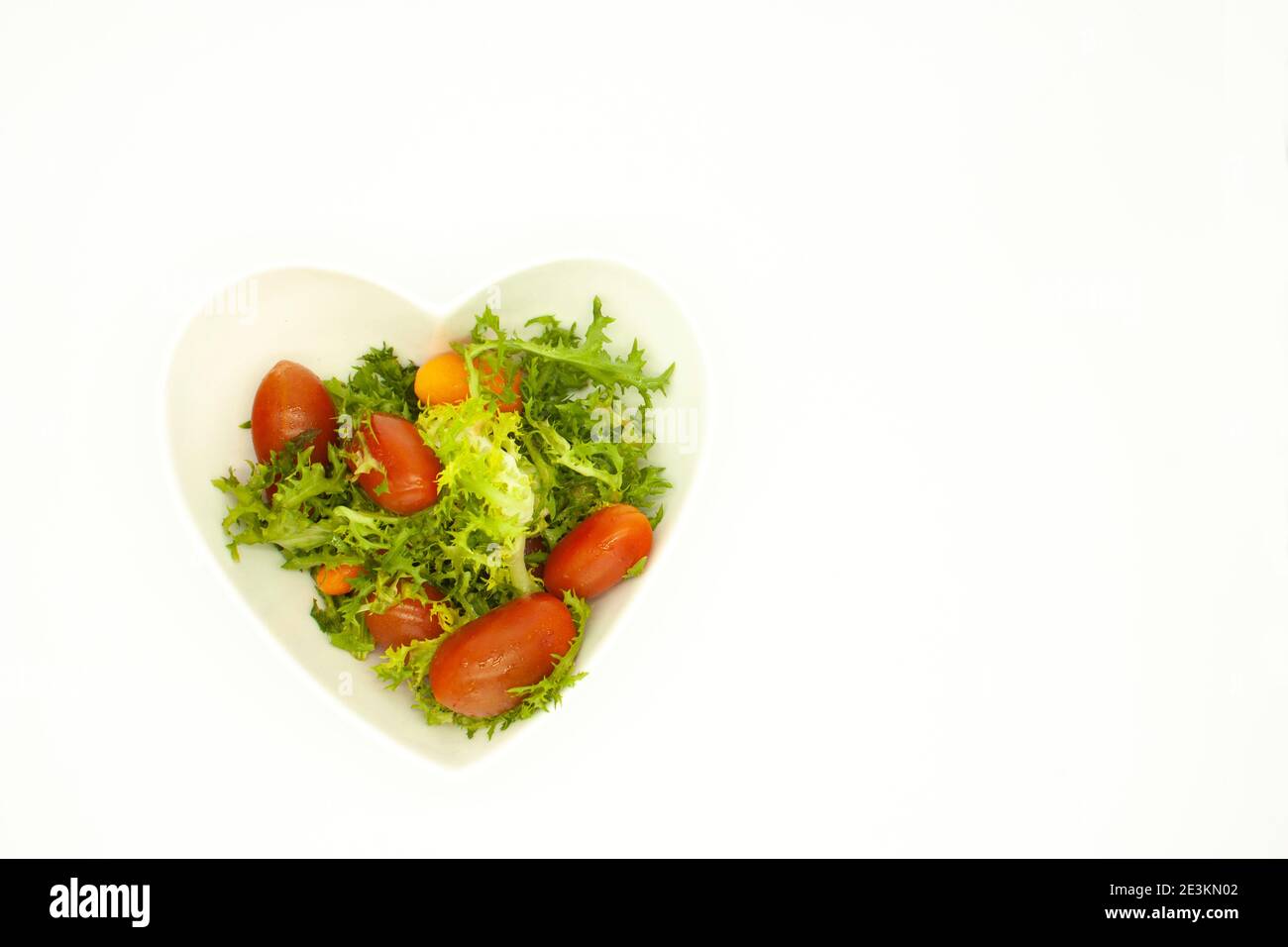 Lattuga mescolata con pomodori ciliegini rossi in una ciotola a forma di cuore cibo vegano biologico Foto Stock