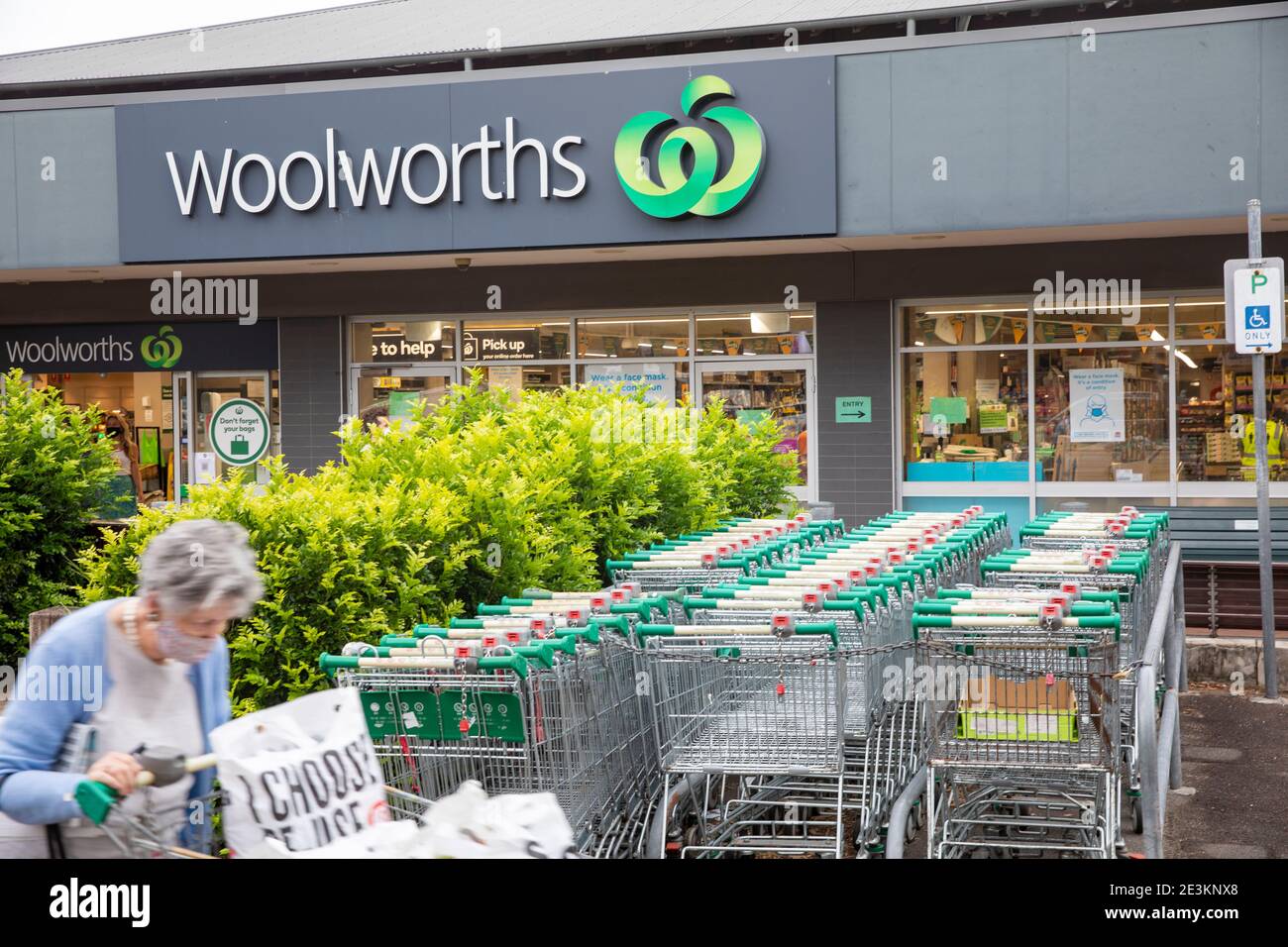 Signora anziana che indossa maschera facciale a causa di COVID 19 foglie Woolworths Supermercato con i suoi negozi, Sydney, NSW, Australia Foto Stock