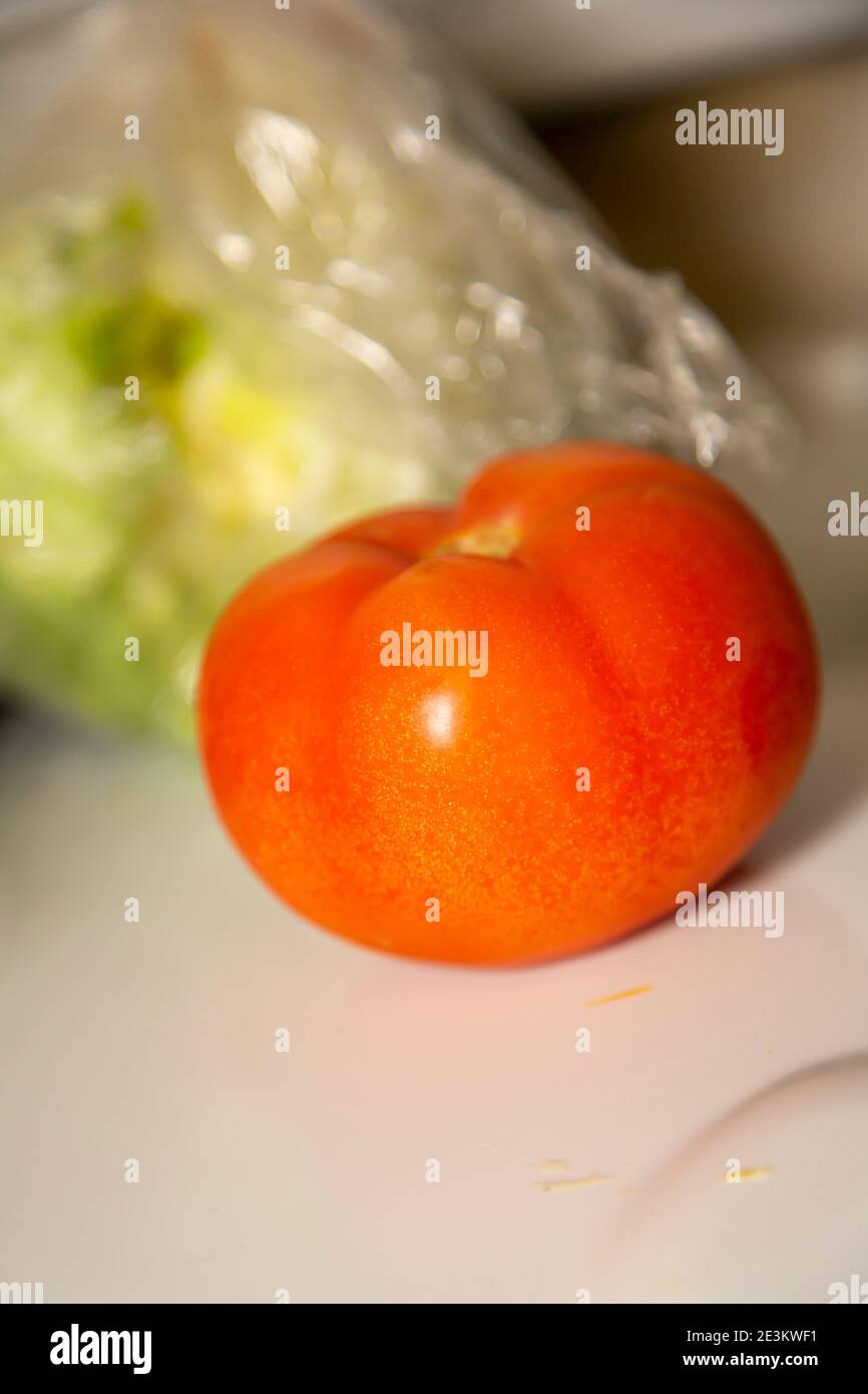 Il pomodoro non tagliato davanti a una testa fuori fuoco di lattuga Foto Stock