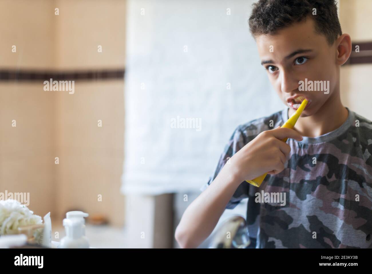 PYoung uomo che gli spazzolava i denti in un bagno di casa, guardando la propria riflessione che si prepara per la scuola Foto Stock