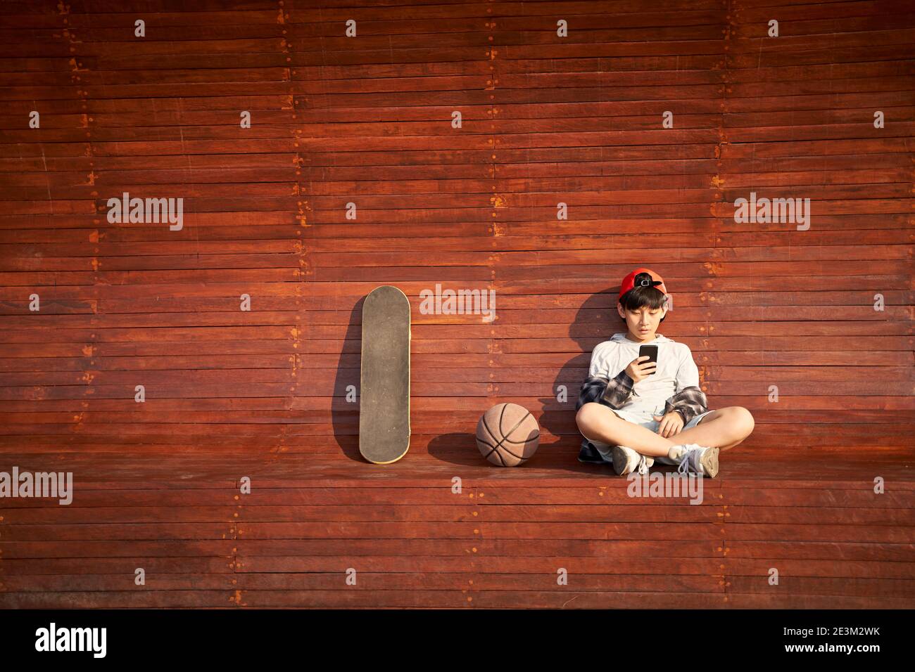 adolescente asiatico skateboarder bambino che guarda il telefono cellulare mentre si riposa Foto Stock