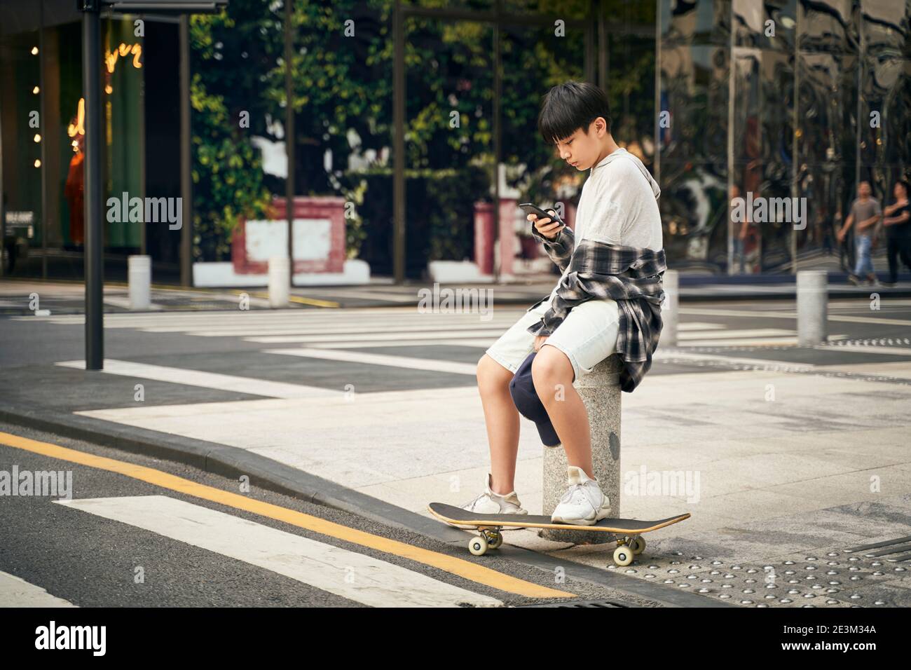 adolescente asiatico skateboarder bambino che guarda il telefono cellulare mentre si riposa Foto Stock