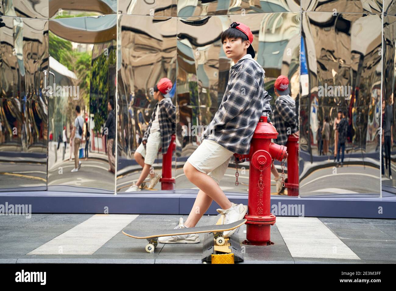 ragazzo asiatico adolescente con skateboard appoggiato contro idrante fuoco su via Foto Stock