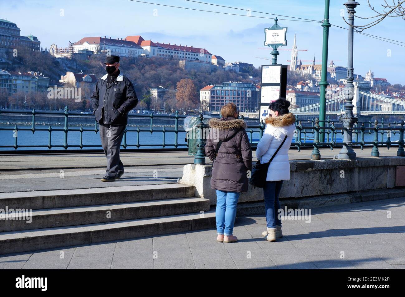 Persone in maschera di fronte in attesa del tram nella stazione del tram sulla riva del Danubio di fronte al panorama Buda a Budapest, Ungheria Foto Stock