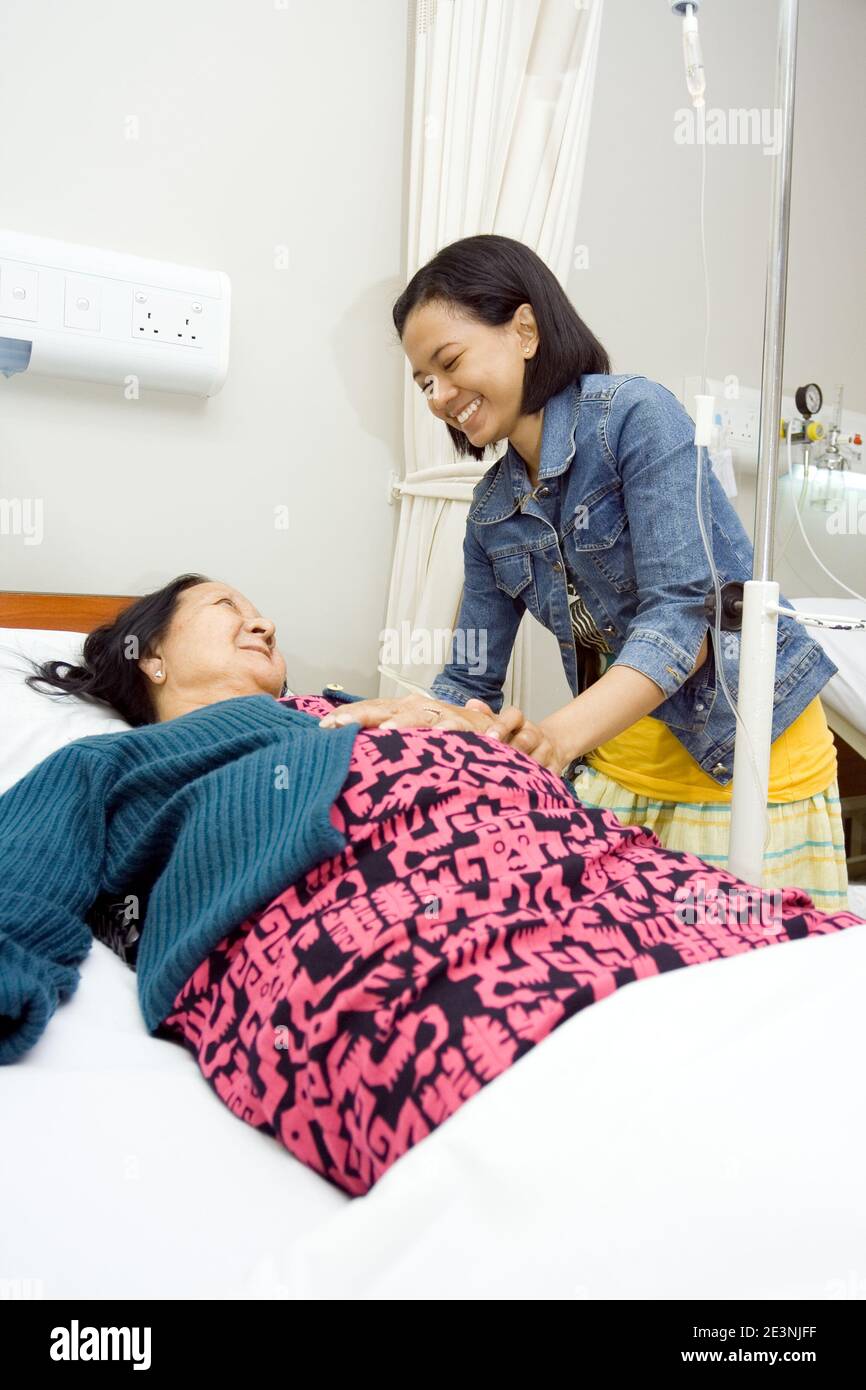 la nonna asiatica malata sembra felice visitata da sua nipote, avendo letto riposandosi in cure ospedaliere Foto Stock