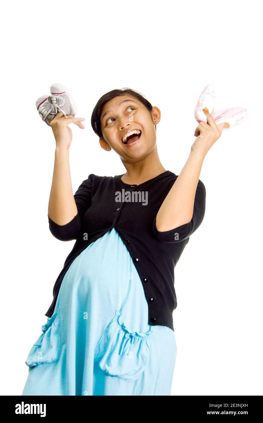 donna asiatica incinta con le coppie delle scarpe del bambino. guardando in su e sorridente felice che sta andando avere i bambini gemelli Foto Stock