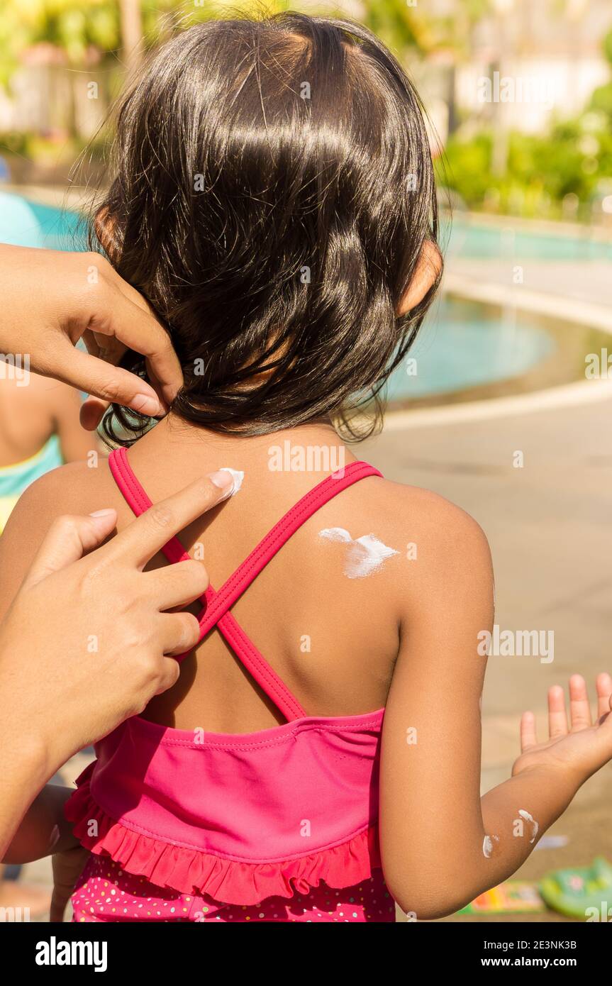 La mano della madre che mette la lozione del Sunblock sulla pelle posteriore della ragazza piccola Prima di nuotare Foto Stock