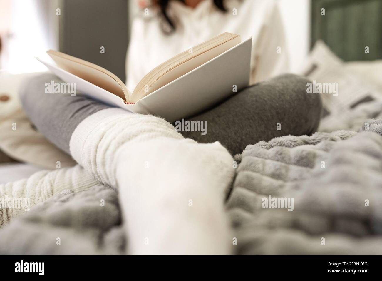 Vista ad angolo basso di una donna irriconoscibile seduta sul divano comodi abiti rilassanti leggendo un libro di carta con lana bianca calzini sfocati in foregroun Foto Stock