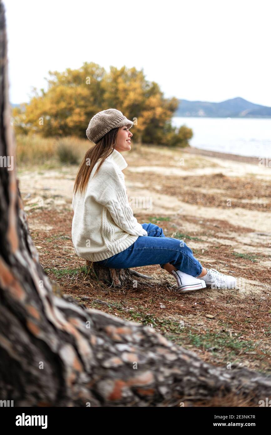 Bella giovane caucasica seduta vicino all'acqua su un tronco d'albero in pineta godendo del magico mare d'inverno. La donna felice vive l'emb Foto Stock
