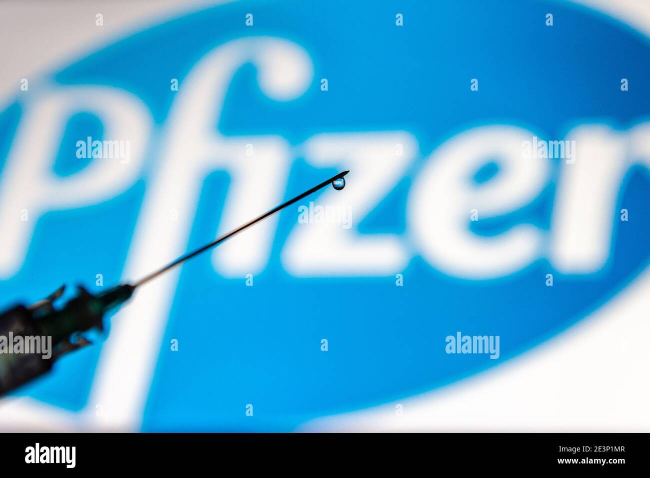 Siringa con una goccia di liquido come vaccino COVID-19 con il logo Pfizer sullo sfondo. Foto Stock