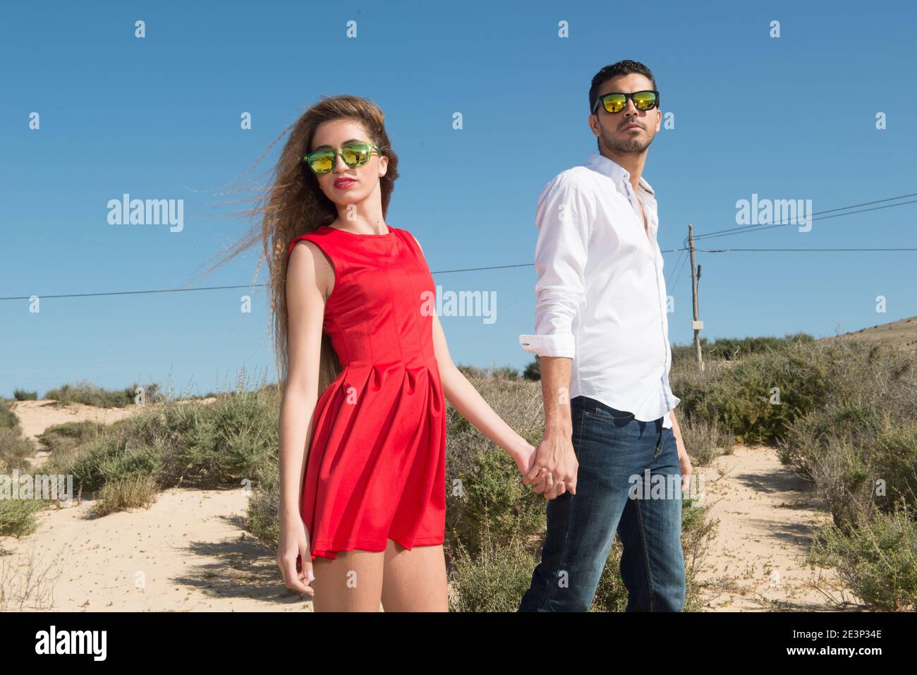 giovane coppia che cammina attraverso un paesaggio desertico sotto il blu cielo Foto Stock