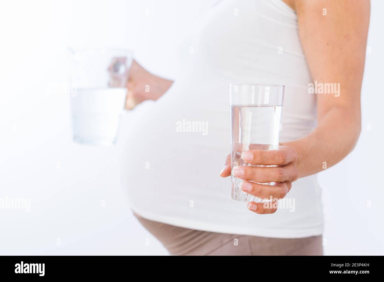 Donna incinta che tiene un bicchiere pieno d'acqua e il vaso su sfondo bianco Foto Stock