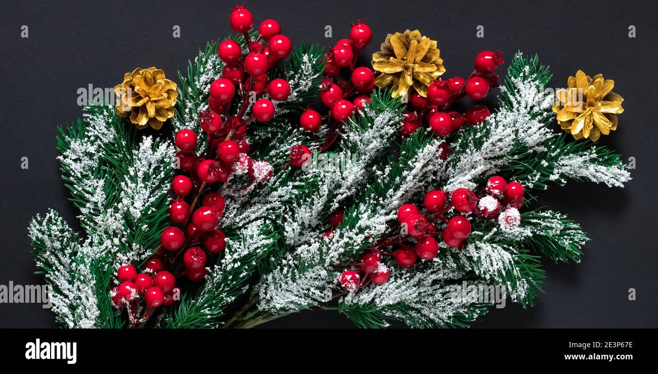 Decorazioni dell'albero di Natale su sfondo scuro. Rami di abete verde con neve, coni di pino dorato e bacche di agrifoglio rosso. Umore di Capodanno, festa invernale Foto Stock