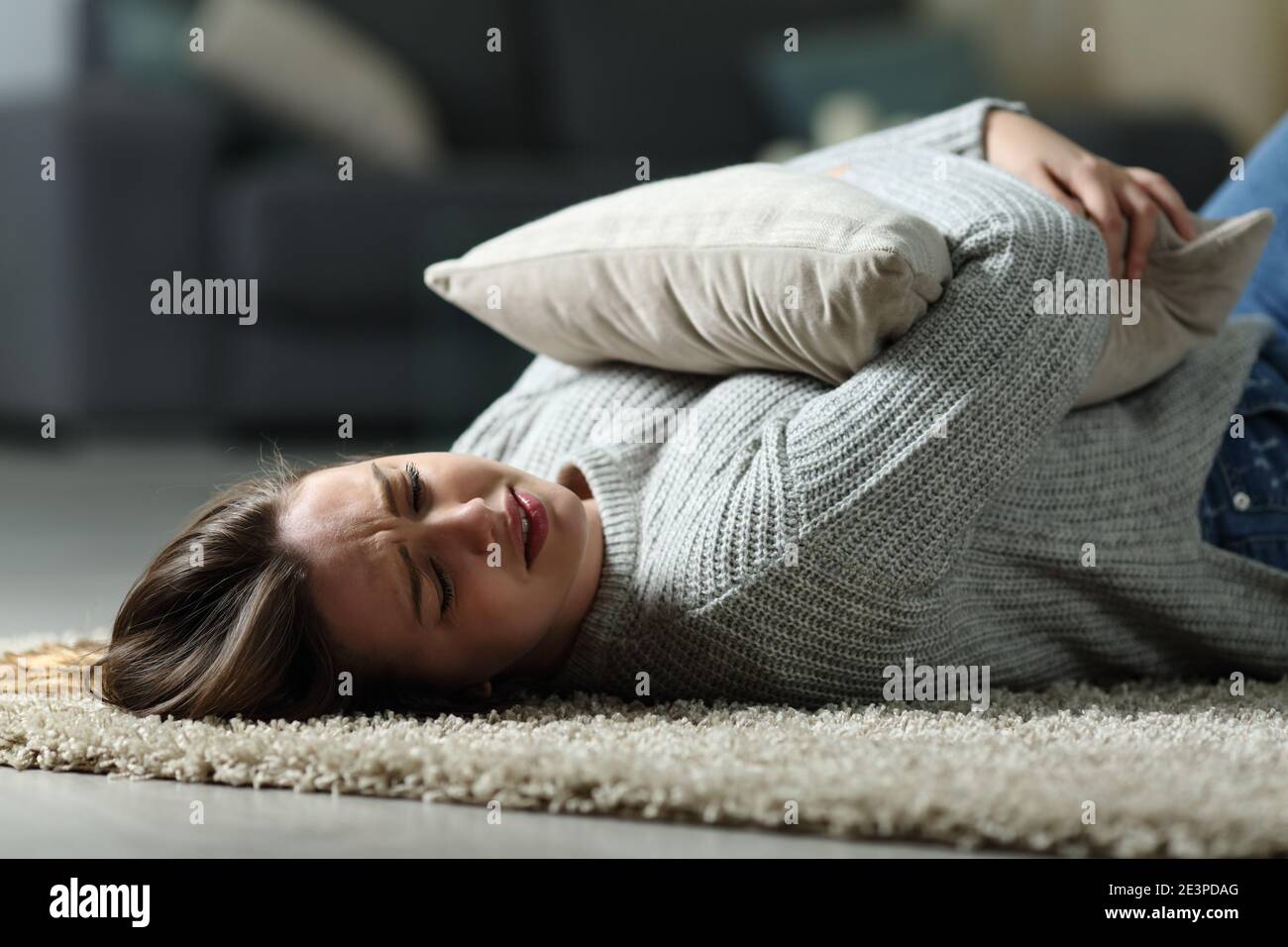 Triste teen lamentando abbracciando cuscino e piangendo sdraiato sul pavimento a casa Foto Stock