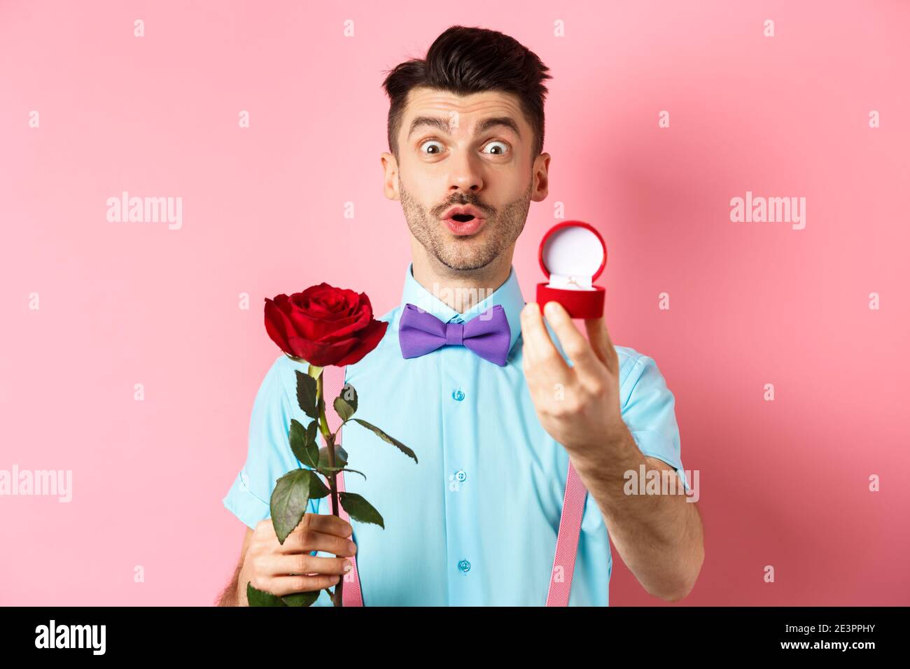 San Valentino. Uomo divertente con baffi e bow-tie facendo proposta,  mostrando anello di impegno e proporre con rosa rossa, in piedi su sfondo  rosa Foto stock - Alamy