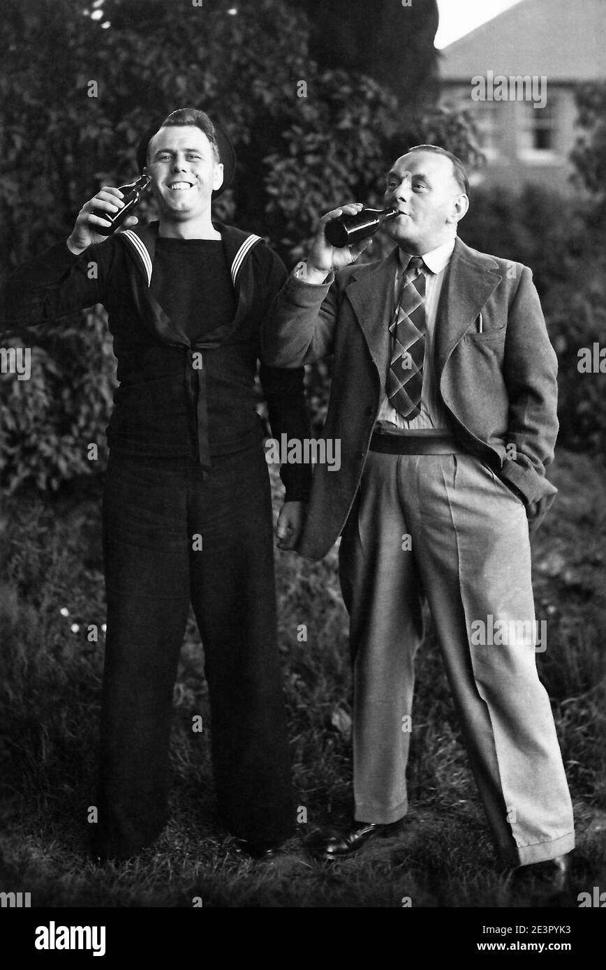 Archivio immagine in tempo di guerra di un padre e di un figlio marinaio godendo le loro bottiglie di birra in giardino. Inghilterra meridionale durante la seconda guerra mondiale. Foto Stock
