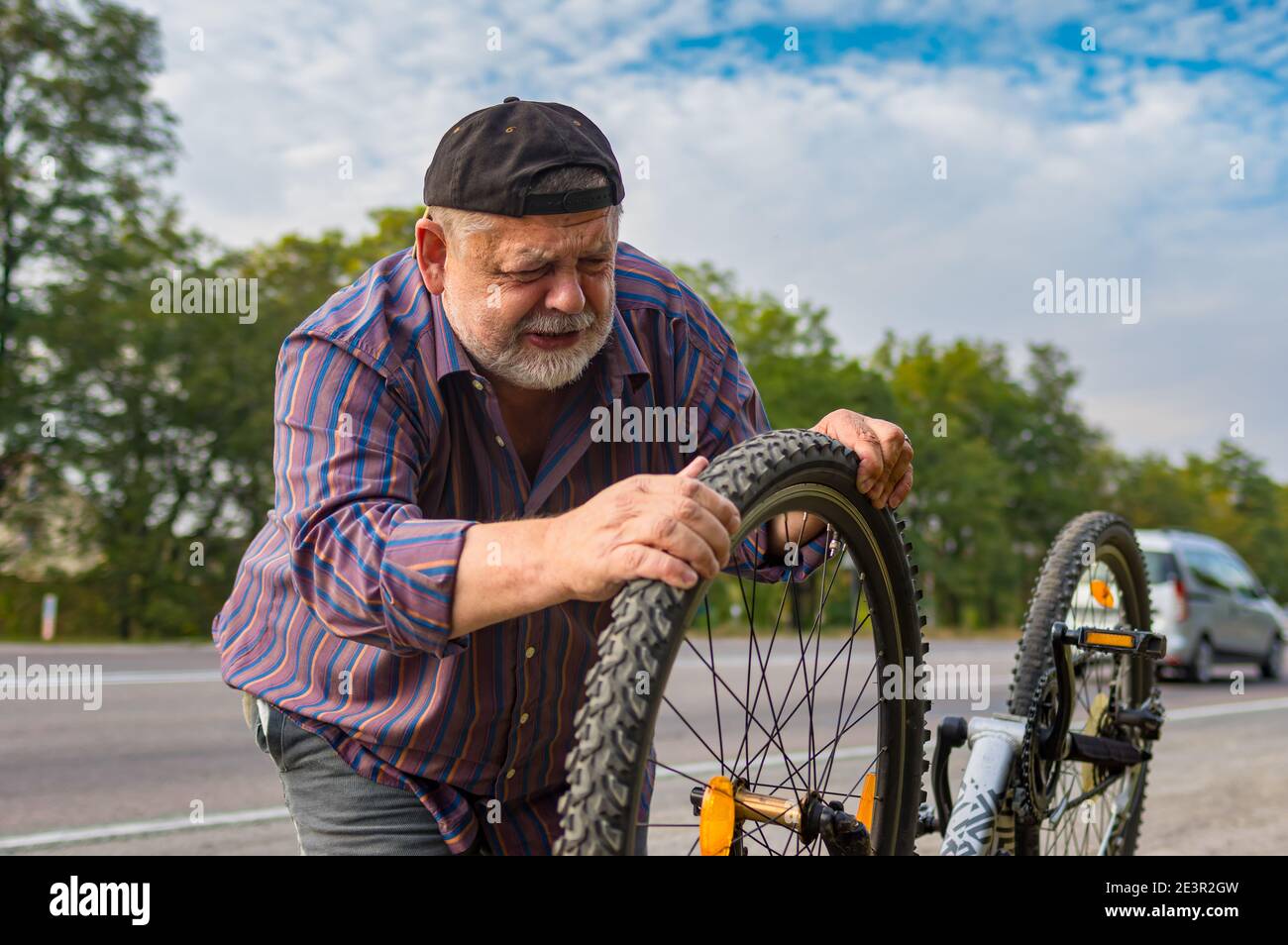 Ritratto esterno dell'uomo caucasico anziano che esamina il pneumatico della bicicletta sopra la strada Foto Stock