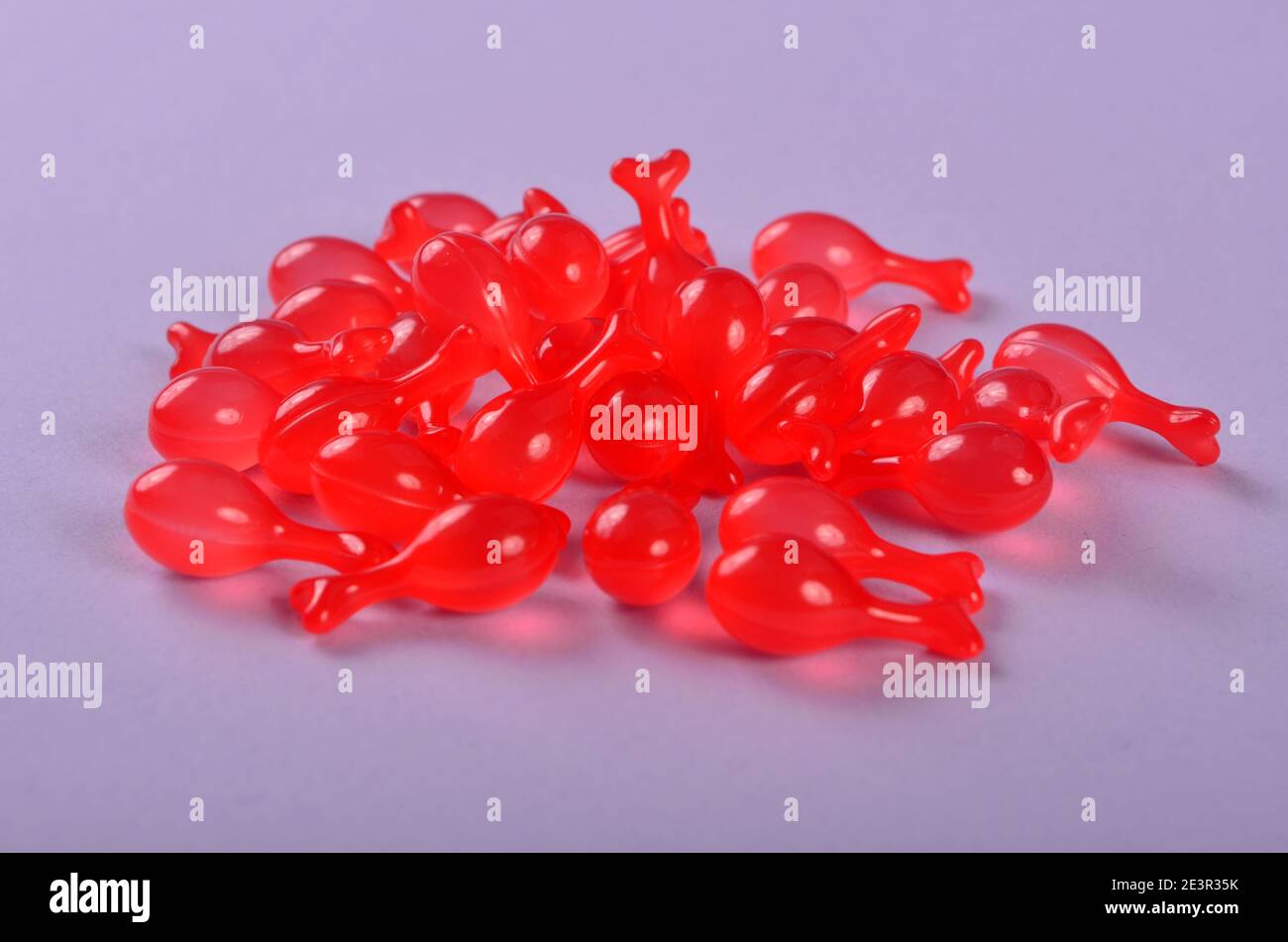 Capsule farmaceutiche di gelatina rossa morbida su sfondo viola. Capsula polipeptidica Caviar Essence liquido diluisce le linee sottili che brigano Foto Stock