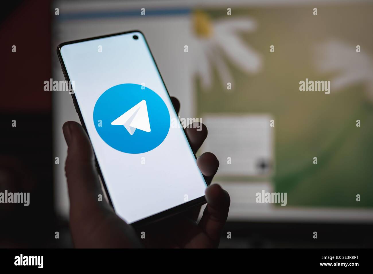 Uomo che ha in mano uno smartphone con il logo dell'app di chat di Telegram Messenger Visualizzato sullo schermo davanti al Web del telegramma versione Foto Stock