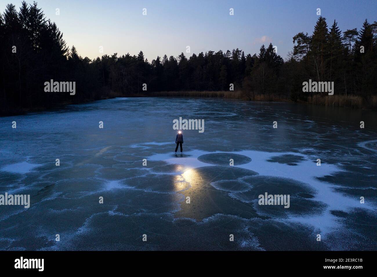 Donna con faro in piedi sul lago ghiacciato al crepuscolo Foto Stock